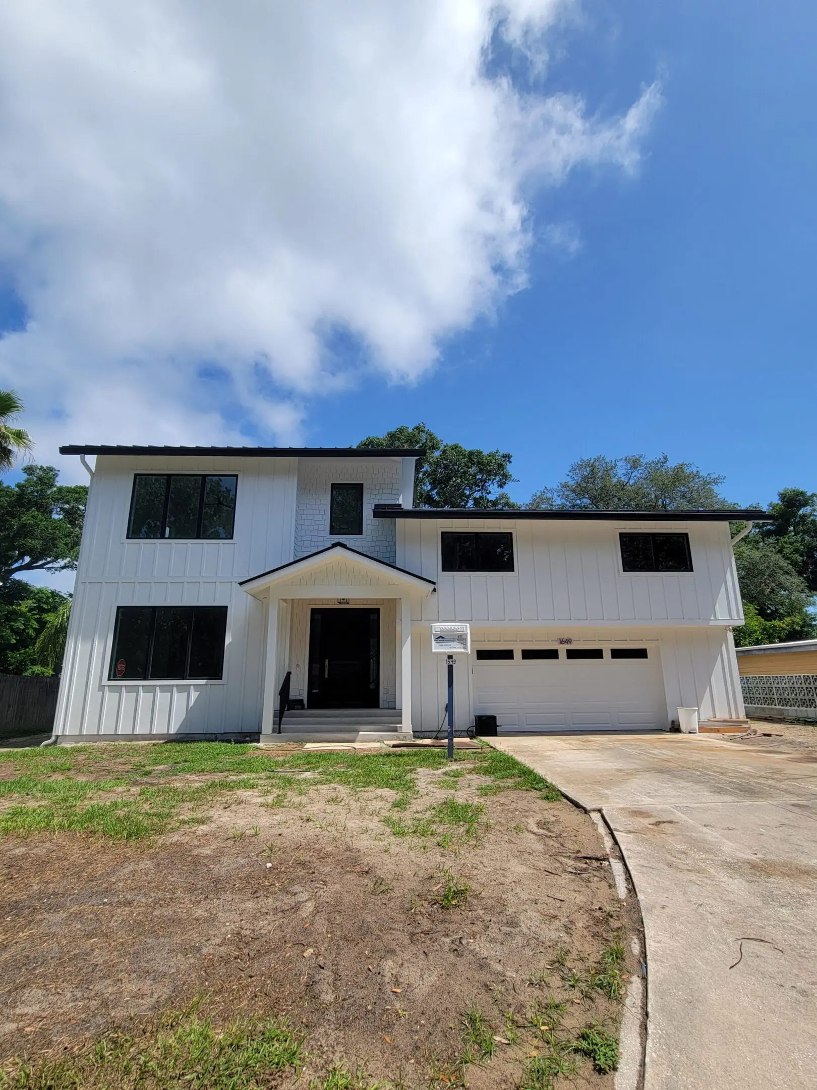Large two-story house with white exterior and attached garage under a partly cloudy sky.